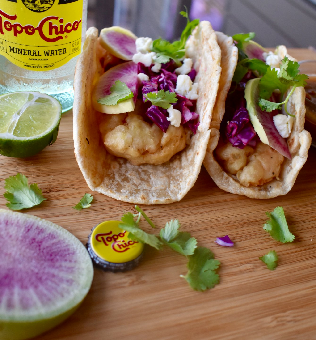 Two crispy fish tacos with cabbage and cilantro on a board.