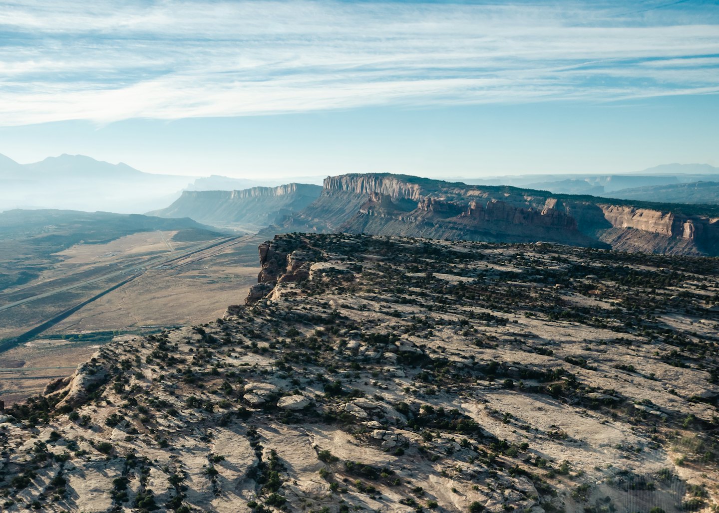 A long road cuts through a desert valley with rugged mesas.