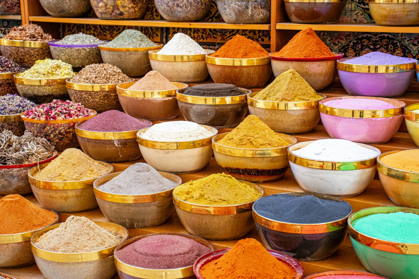 Small bowls filled with colorful spices arranged on wooden shelves.
