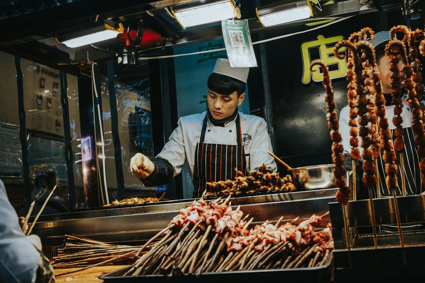 Chef preparing skewers at a busy street food stall at night.