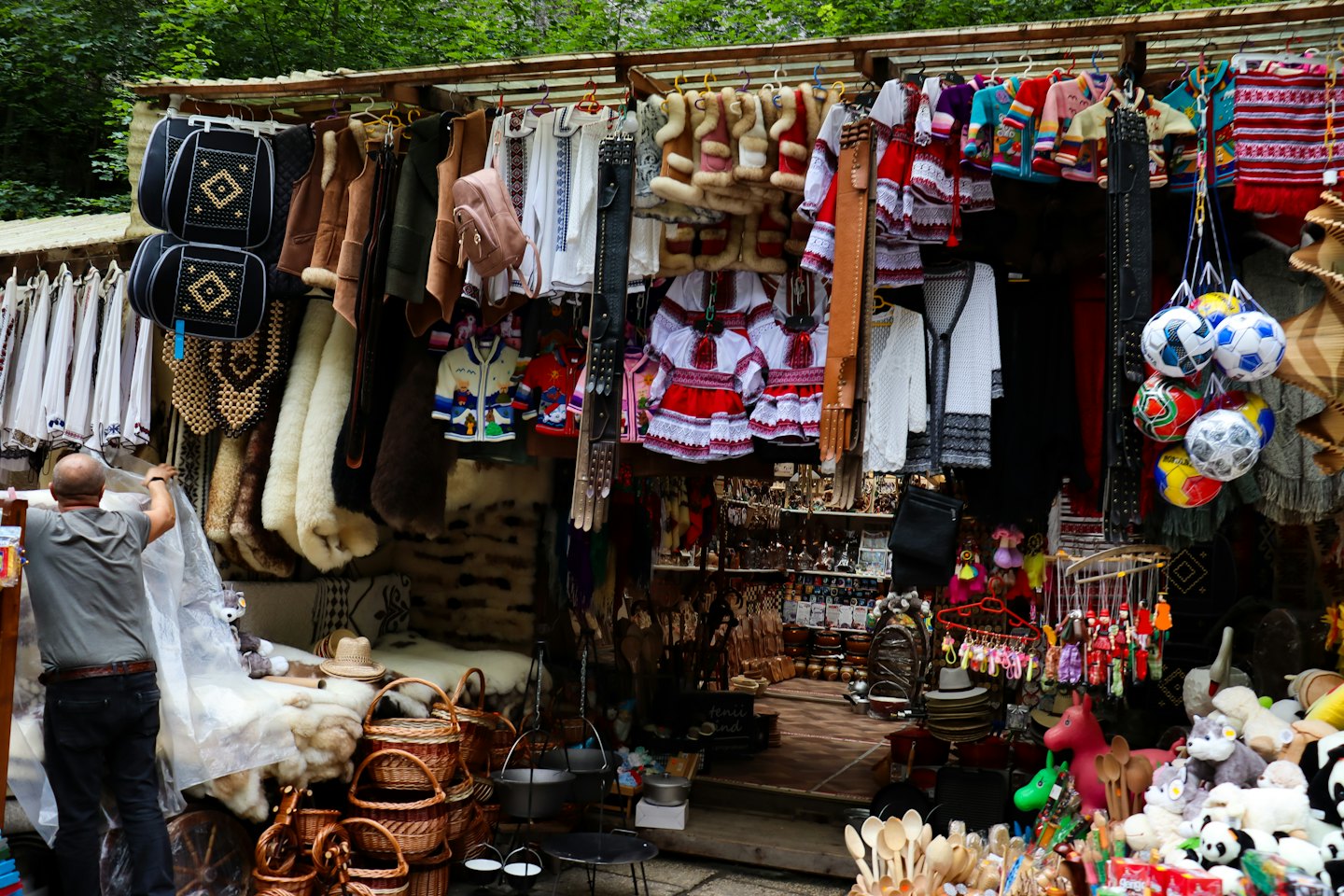 Vendor adjusts protective plastic over crafts at an outdoor stall.