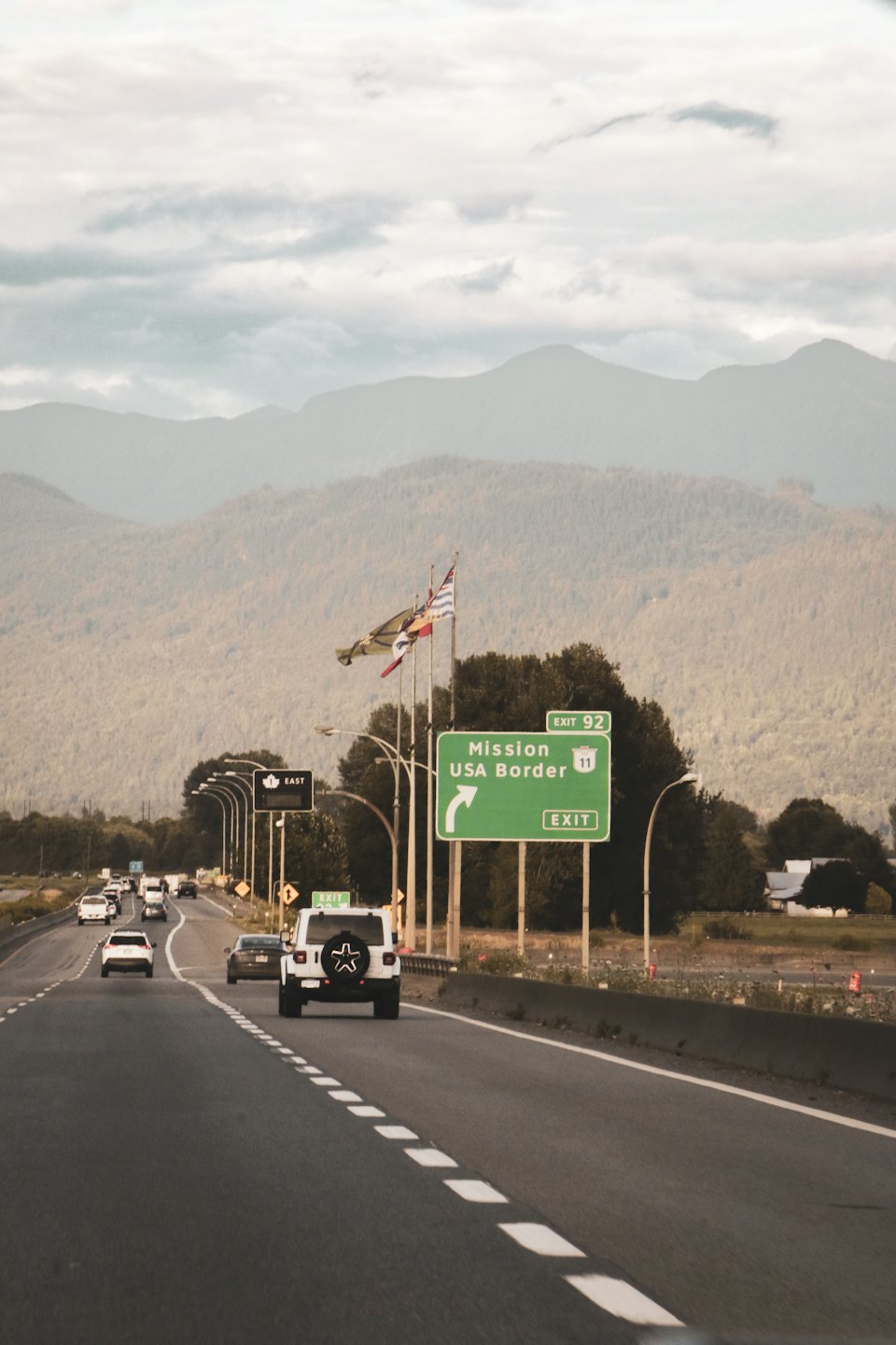 Cars driving on the highway towards a green border sign.