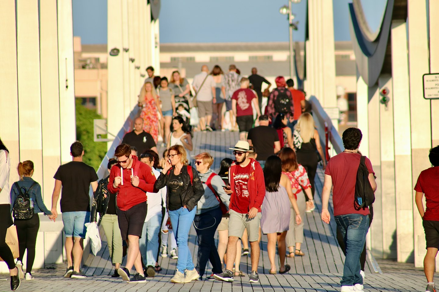 People walk across a modern pedestrian bridge in the city.