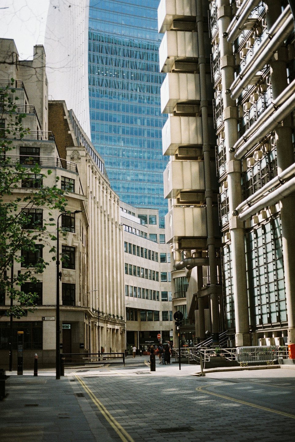 People walk on a city street between historical and modern buildings.
