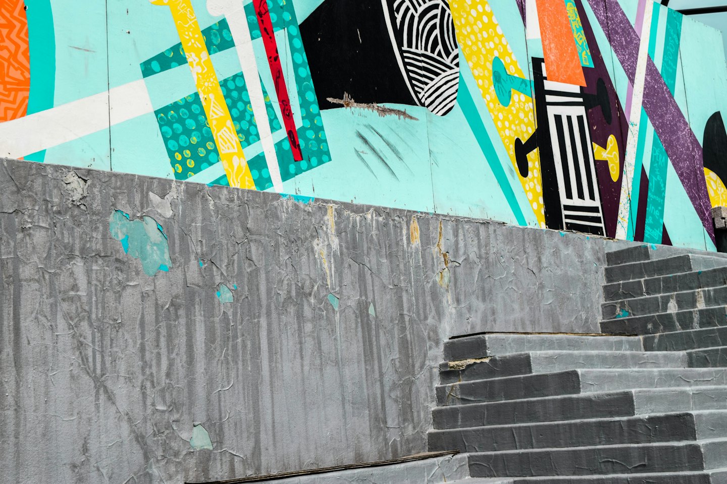 Abstract geometric mural on a wooden fence above concrete.
